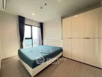 Modern bedroom with city view, featuring sleek wardrobe and large window for natural light.
