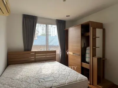 Cozy bedroom with large window and wooden furniture, offering a serene view of the cityscape.