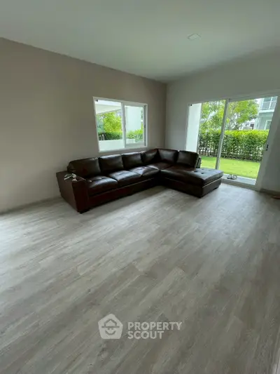 Spacious living room with modern flooring and garden view, featuring a stylish leather sectional sofa.