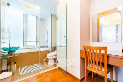 Modern bathroom with glass shower, bathtub, and wooden vanity desk.
