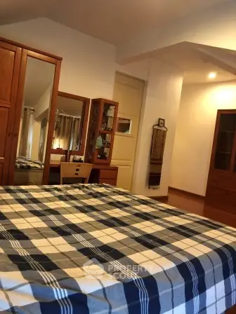 Spacious bedroom with wooden furniture and plaid bedding, perfect for cozy living.