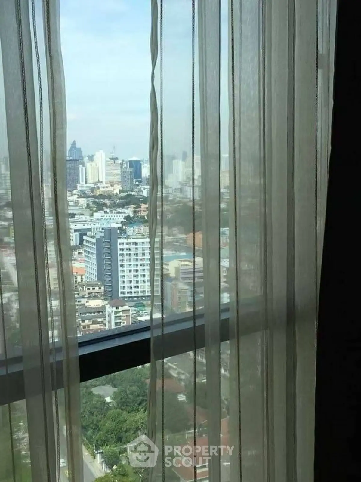 Stunning cityscape view from high-rise apartment window with sheer curtains.