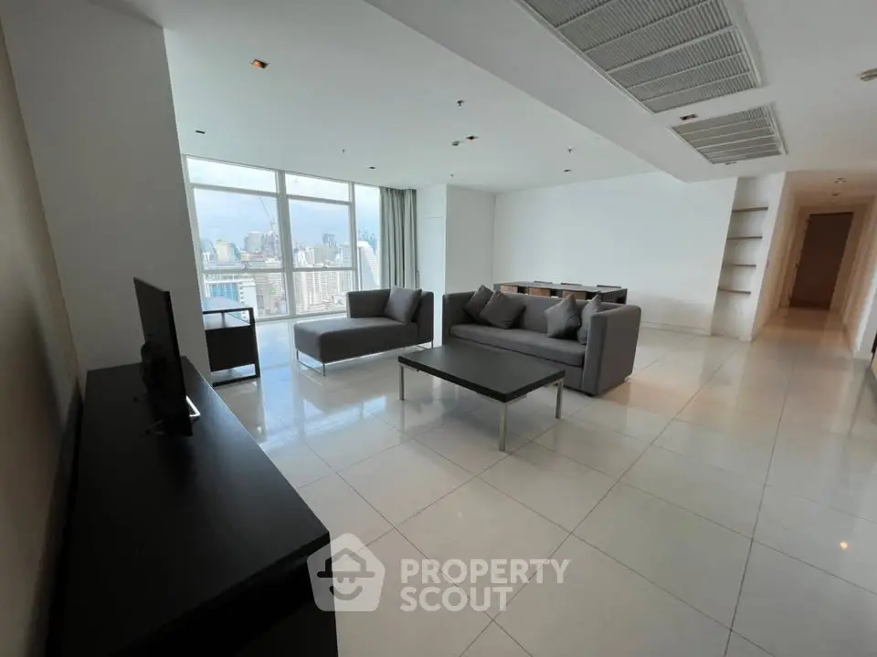 Spacious modern living room with city view, featuring sleek furniture and large windows.