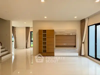 Spacious modern living room with built-in wooden entertainment unit and large windows.