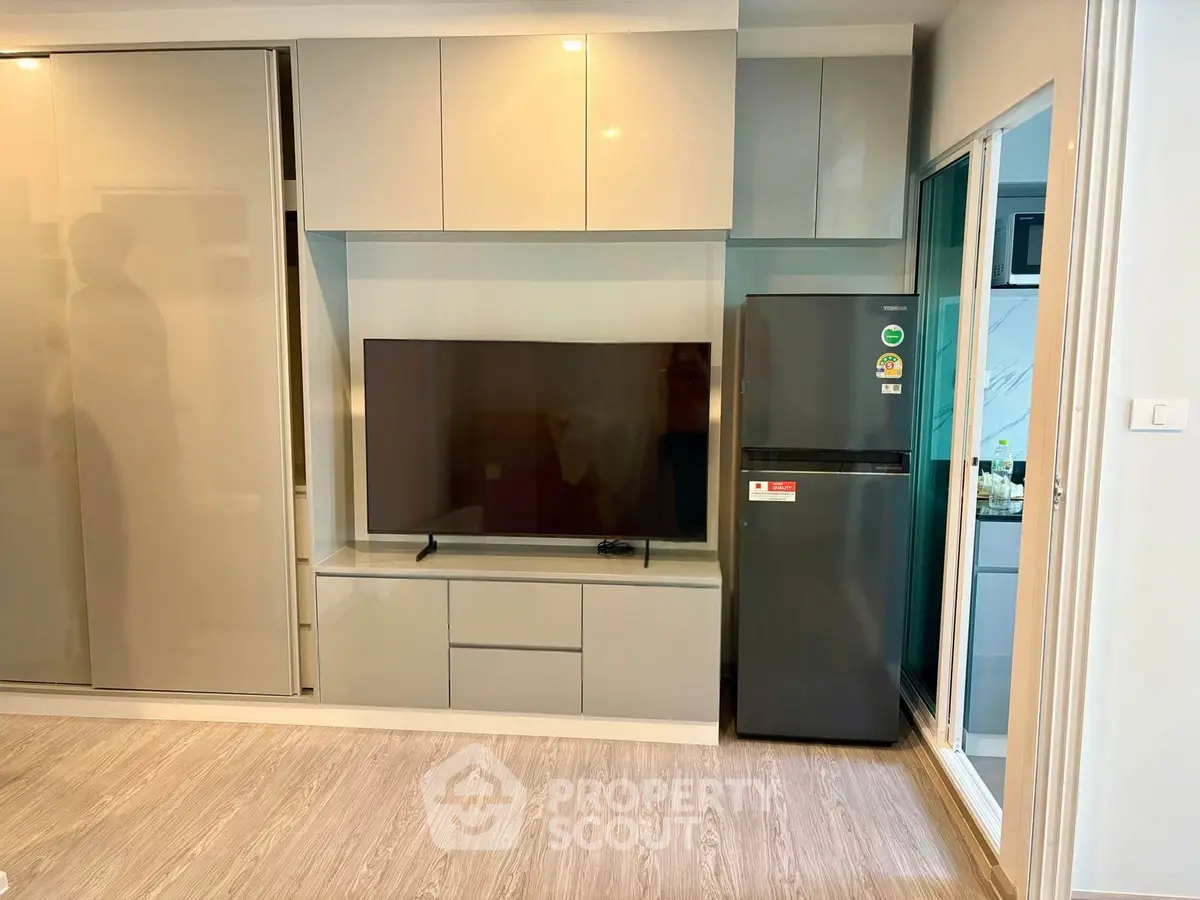 Modern living room with sleek cabinetry and a large TV, adjacent to a compact kitchen area.