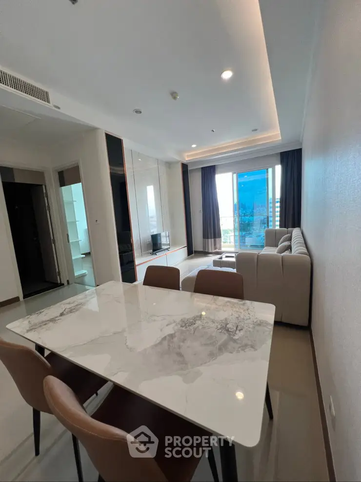 Modern living room with marble dining table and large windows offering city views.