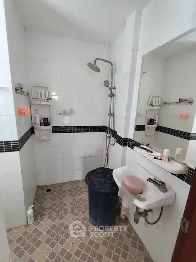 Modern bathroom with shower and sink in a tiled interior, featuring a sleek design and practical storage solutions.