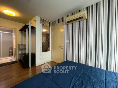 Modern bedroom with striped wallpaper and air conditioning, featuring a view into an ensuite bathroom.