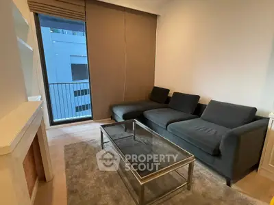 Modern living room with sleek black sofa and glass coffee table, featuring a small balcony view.