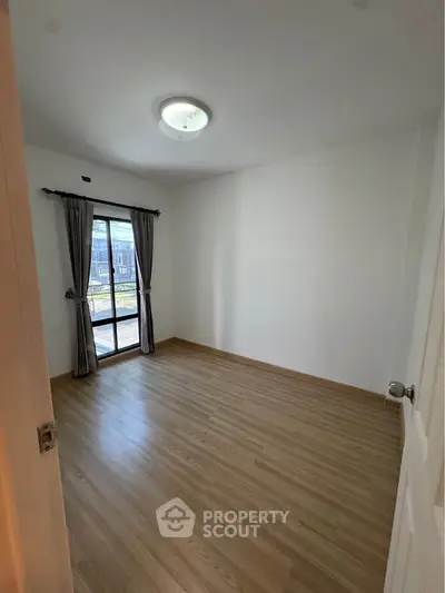 Spacious empty bedroom with wooden flooring and large window