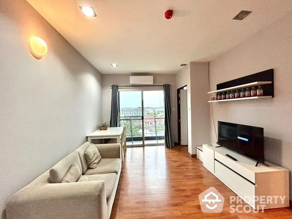 Modern living room with balcony and city view, featuring sleek furniture and wooden flooring.