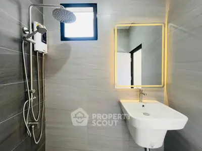 Modern bathroom with sleek fixtures and illuminated mirror, featuring a rainfall showerhead and stylish sink.