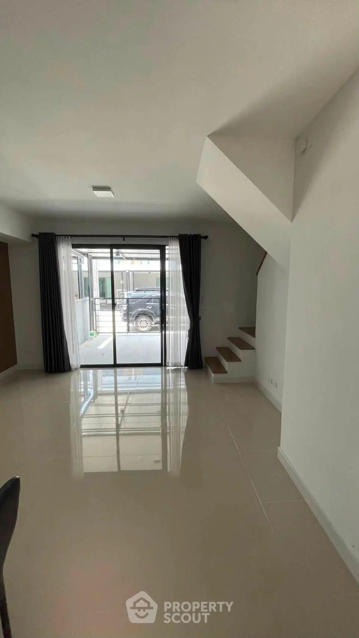 Spacious modern living room with glossy tiled floors and large windows leading to outdoor area.