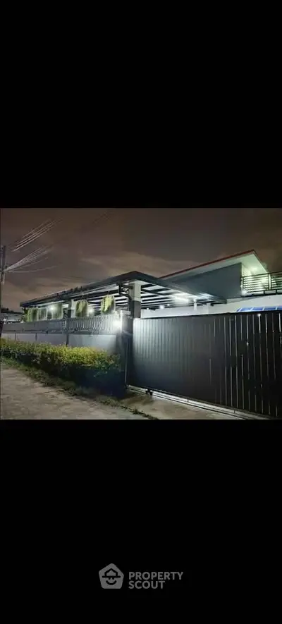 Modern single-story house with sleek fence and ambient lighting at night.