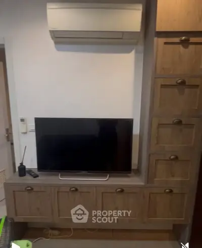 Modern living room with built-in wooden cabinets and wall-mounted TV under air conditioning unit.