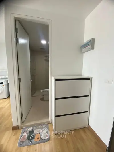 Modern apartment interior with bathroom and washing machine, featuring sleek storage and wooden flooring.