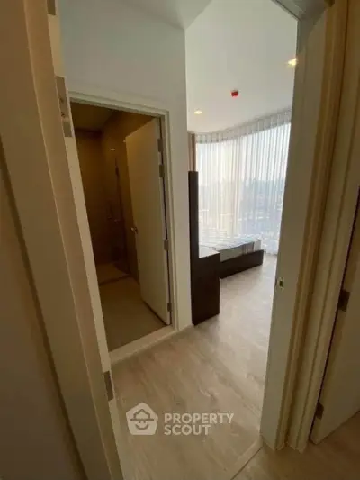 Modern apartment hallway leading to a bright bedroom with large windows and wooden flooring.