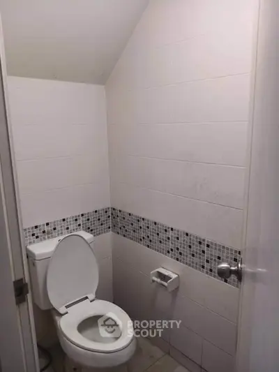 Compact bathroom with white tiles and mosaic accent wall, featuring a standard toilet and minimalistic design.