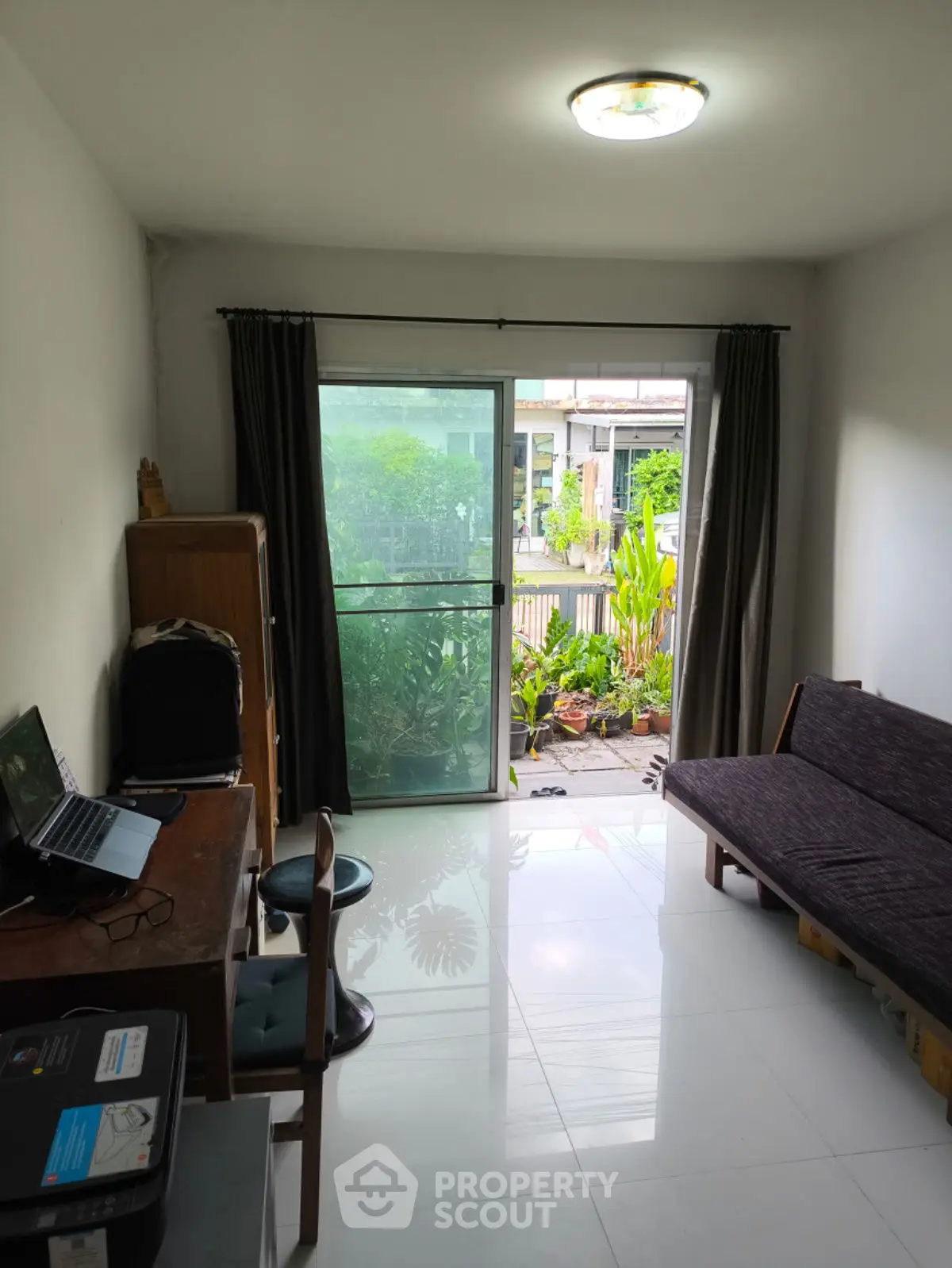 Cozy living room with garden view, featuring a desk and sofa, ideal for work-from-home setup.