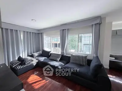 Spacious living room with large windows and modern sectional sofa in a bright apartment.