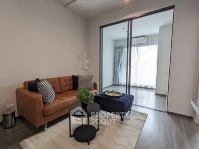 Chic modern living room with elegant brown sofa, stylish blue ottoman, sleek black coffee tables, and large sliding glass doors leading to a sunlit balcony.