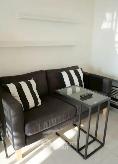 Cozy living room with modern black sofa and glass-top table, perfect for relaxation.