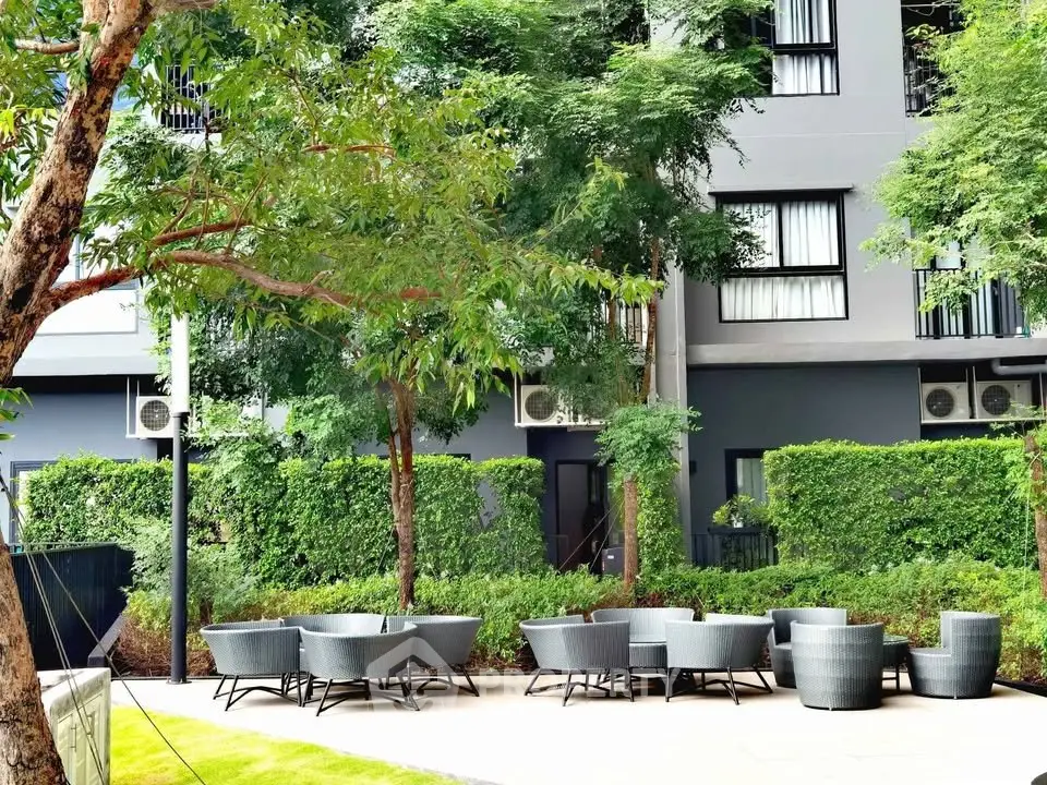Modern apartment building exterior with lush greenery and stylish outdoor seating area.
