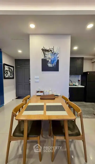 Modern dining area with wooden table and chairs, adjacent to a sleek kitchen in a stylish apartment.