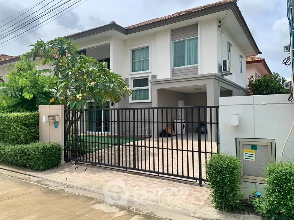 Modern two-story house with gated entrance and lush greenery