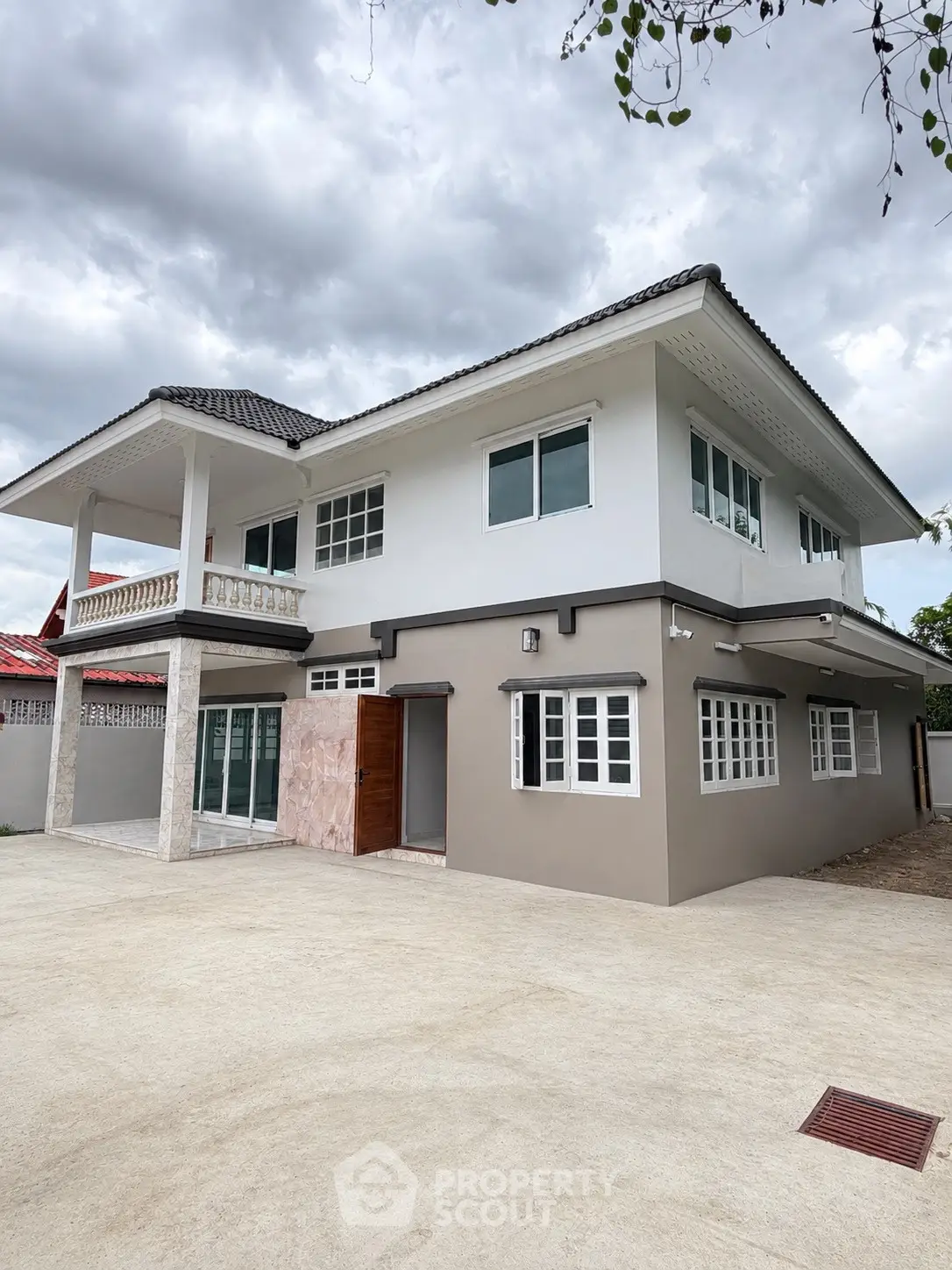 Modern two-story house with spacious driveway and elegant balcony under cloudy sky.