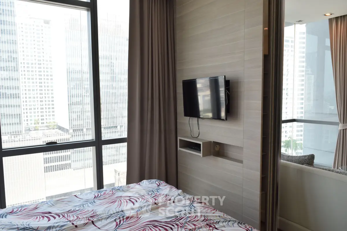 Modern bedroom with city view, featuring a wall-mounted TV and large windows for natural light.