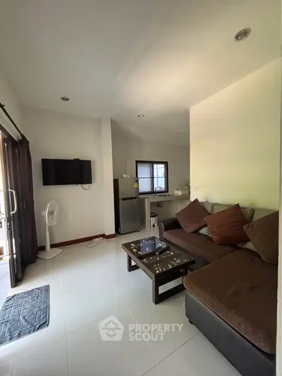Cozy living room with modern decor, featuring a comfortable sofa, wall-mounted TV, and a compact kitchen area.