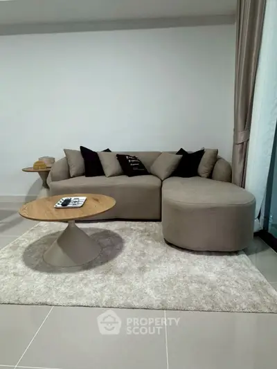 Modern living room with stylish beige sofa and round coffee table on plush rug.