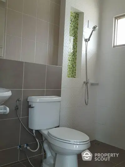 Pristine bathroom with modern fixtures, neutral tilework, and a splash of green mosaic for a refreshing touch, ideal for contemporary living.