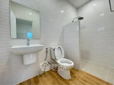 Modern bathroom with sleek white tiles and wooden flooring, featuring a shower and toilet.