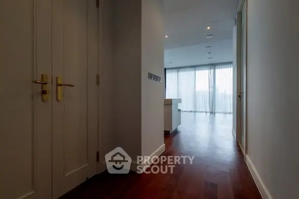 Spacious hallway with wooden flooring leading to a bright living area with large windows.