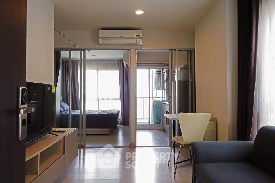 Modern apartment interior with open living room and bedroom, featuring sleek furniture and natural light.