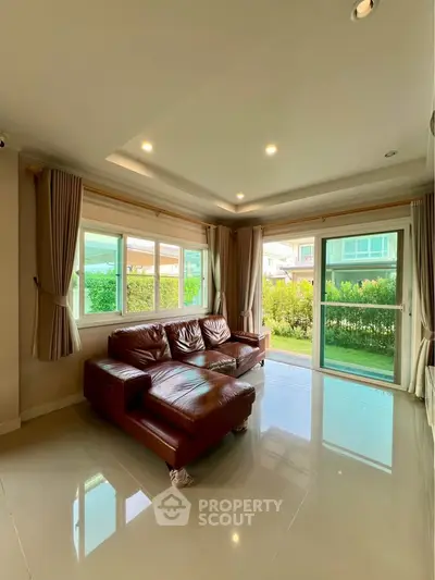 Spacious living room with leather sofa and large windows overlooking garden.