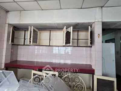 Spacious kitchen with open cabinets and tiled countertops, ideal for renovation opportunities.