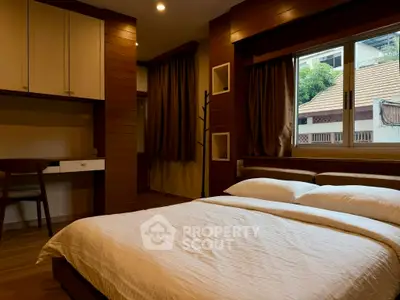 Cozy bedroom with wooden accents and large window offering natural light.