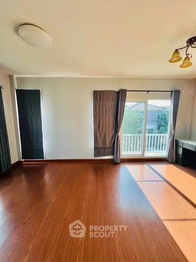 Spacious empty room with wooden flooring and large windows offering natural light.