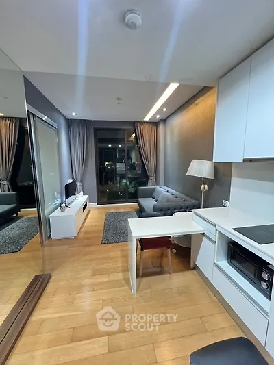 Modern living room with sleek kitchen and cozy seating area, featuring elegant lighting and hardwood floors.