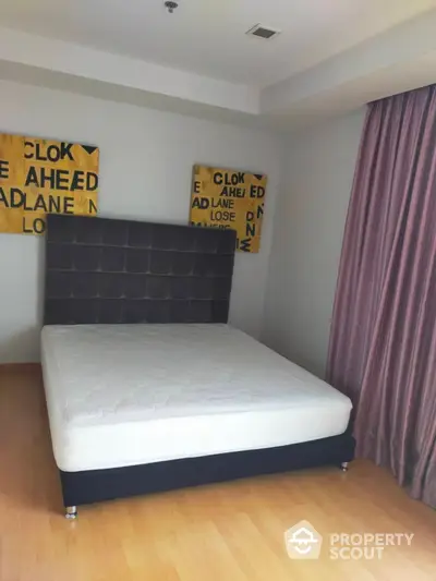 Spacious bedroom with a large bed, hardwood floors, and unique yellow street sign wall art, complemented by elegant purple curtains.