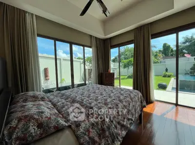 Spacious bedroom with garden and pool view, featuring large windows and elegant decor.