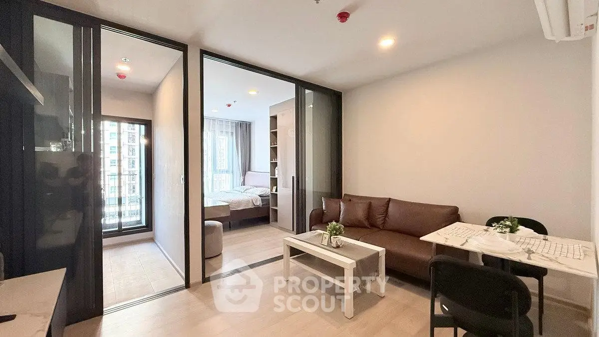 Modern apartment interior with open living room and bedroom, featuring sleek furniture and natural light.