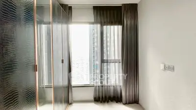 Modern bedroom with large window and sleek wardrobe in high-rise apartment.