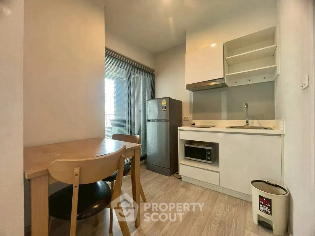 Modern kitchen with compact design, featuring a fridge, microwave, and dining area in a cozy apartment.