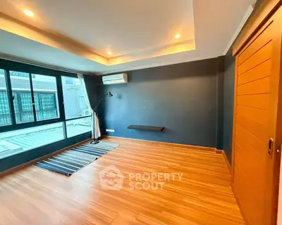 Spacious empty room with wooden flooring and large windows, perfect for customization.