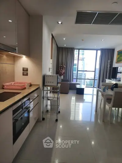 Modern open-layout kitchen and living room with large windows and sleek furnishings.