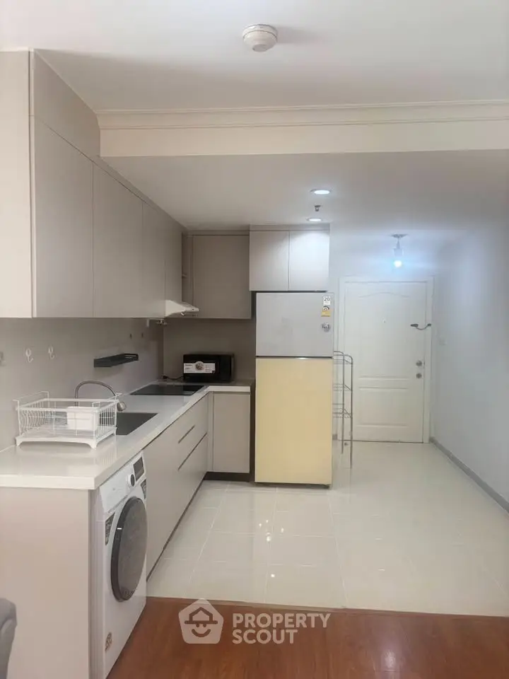 Modern kitchen with sleek cabinetry, washing machine, and fridge in a bright apartment.
